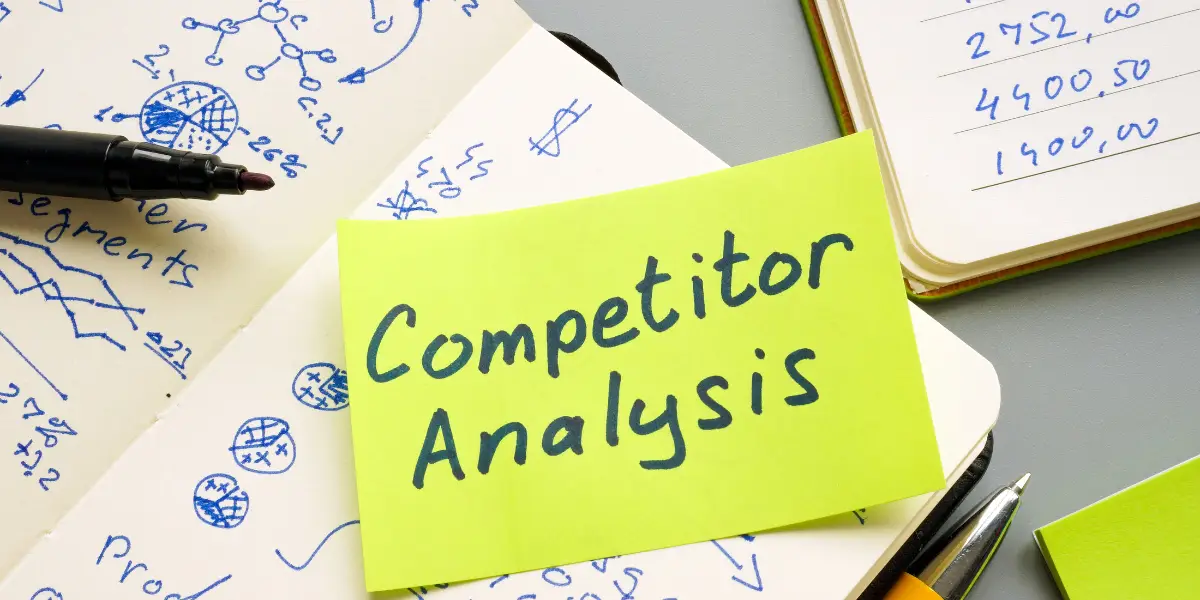 a yellow sticky note sat on a notebook with text saying competitor analysis